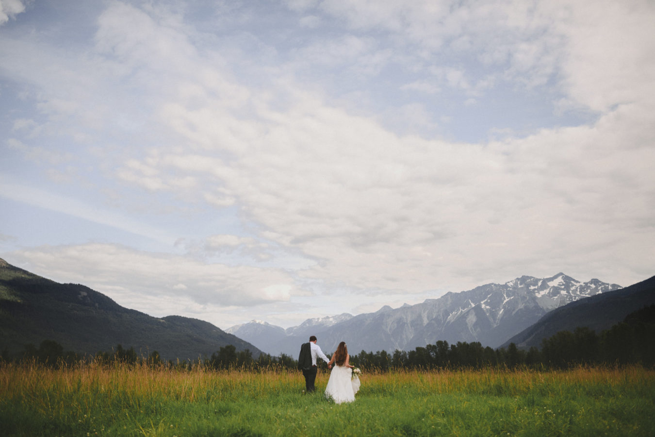 bride and groom walking in a huge field towards the mountains in front of them framed by a big sky