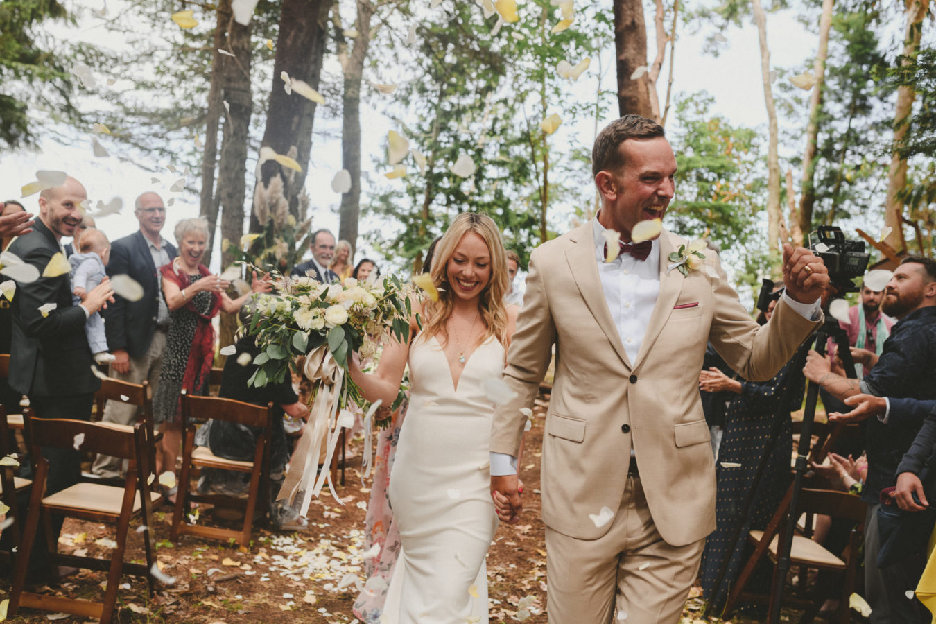 bride and groom walking up the aisle under thrown flower petals smiling and laughing with joy