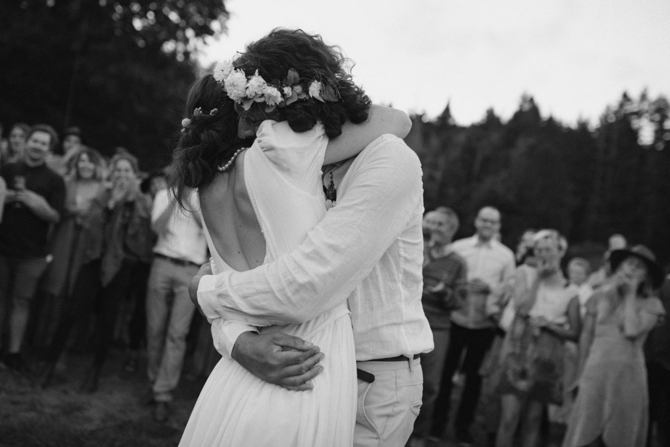 intimate moment of bride and groom hugging tightly just after their first dance with their guests cheering in the background