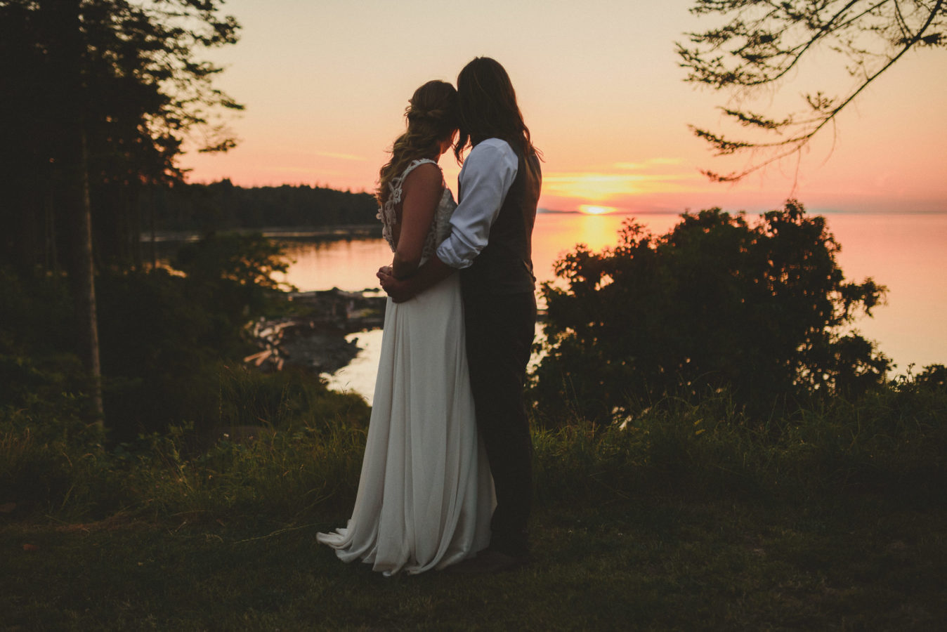 bride and groom hugging looking out at the setting sun over a bay