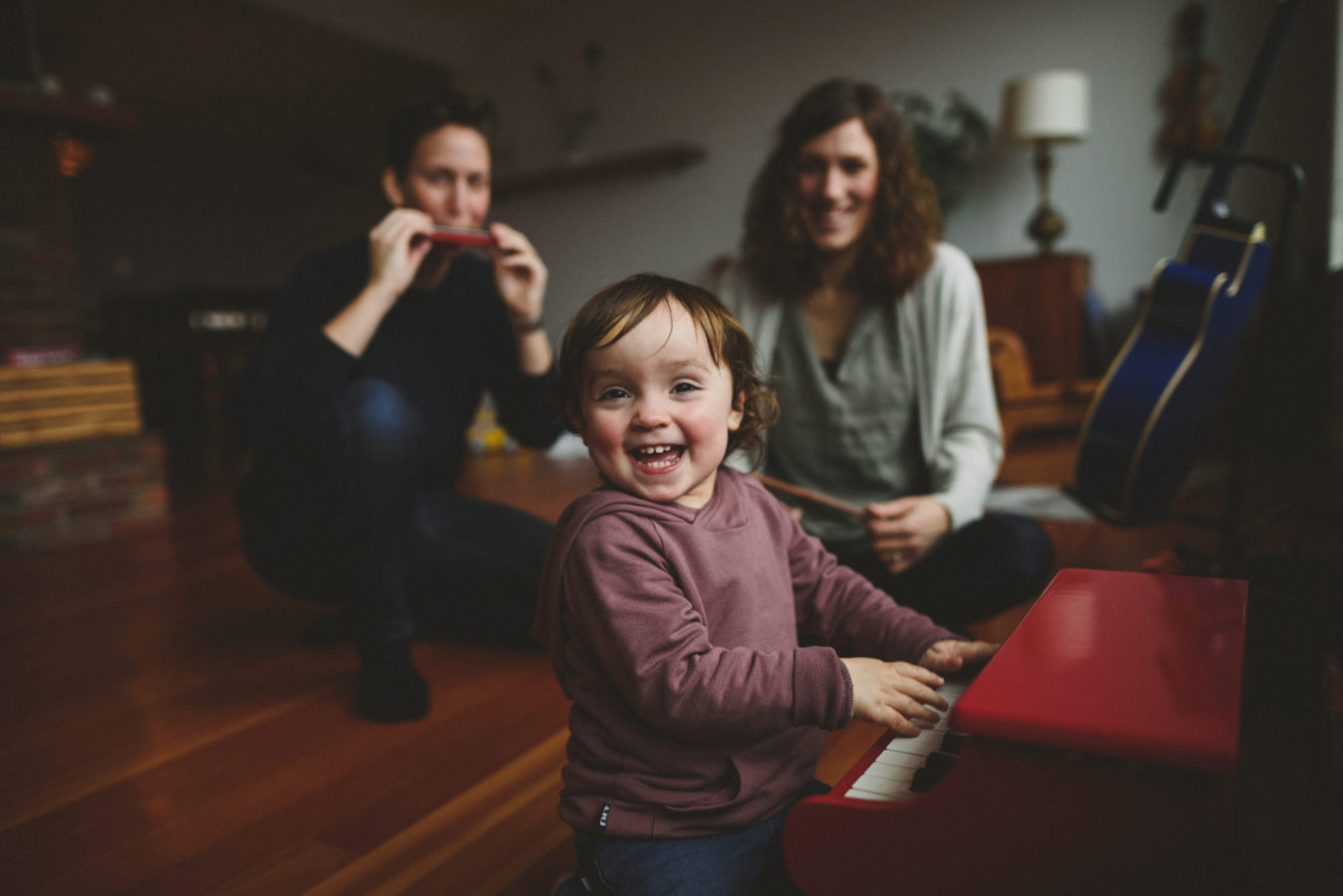 kid laughing while playing a toy piano and her mom's out of focus playing instruments in the background