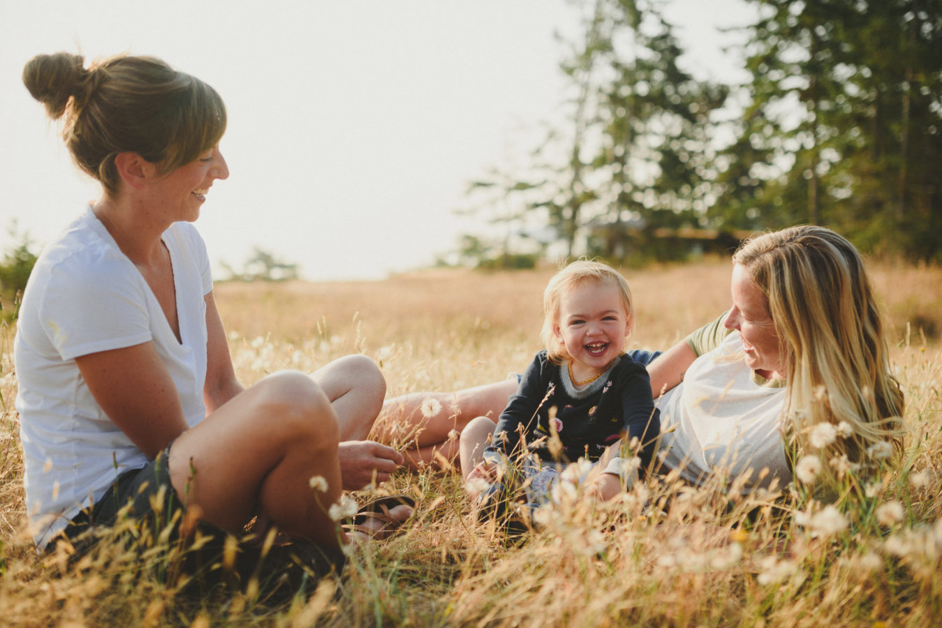 two moms and their daughter laying in the tall grassy on a sunny morning