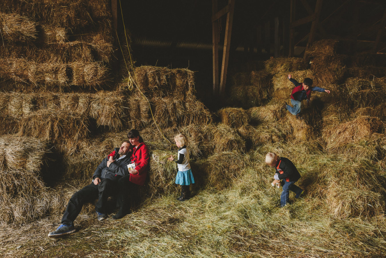 family amongst the hay bails in a bar with one kid jumping in the air
