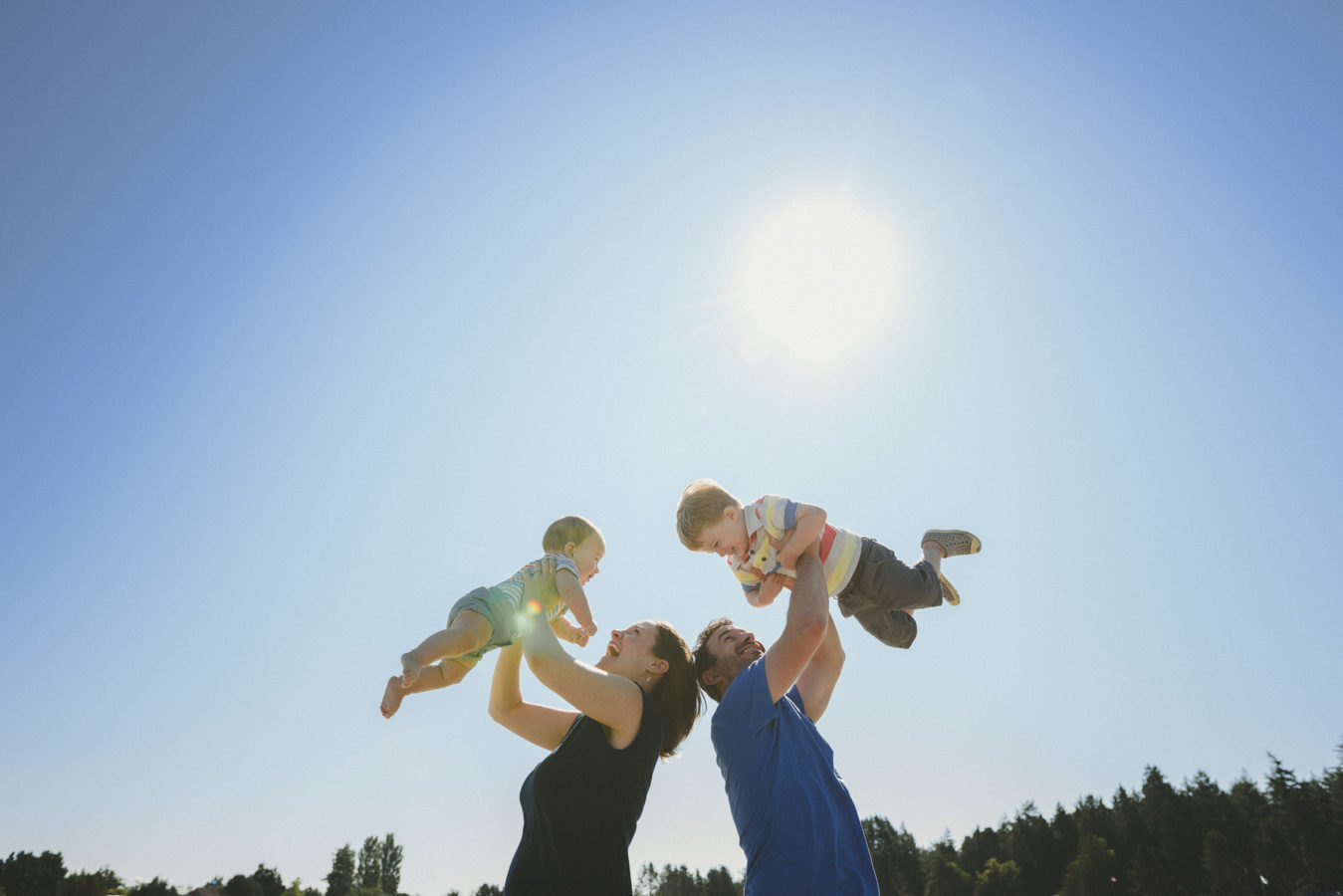 mom and dad holding their little kids up over their heads with the sun shining behind them