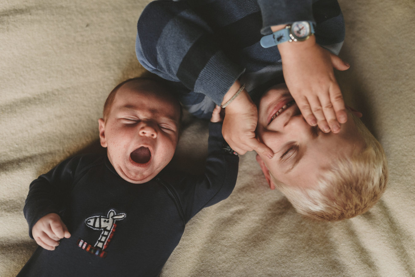 looking down on a baby and kid lying on a bed together