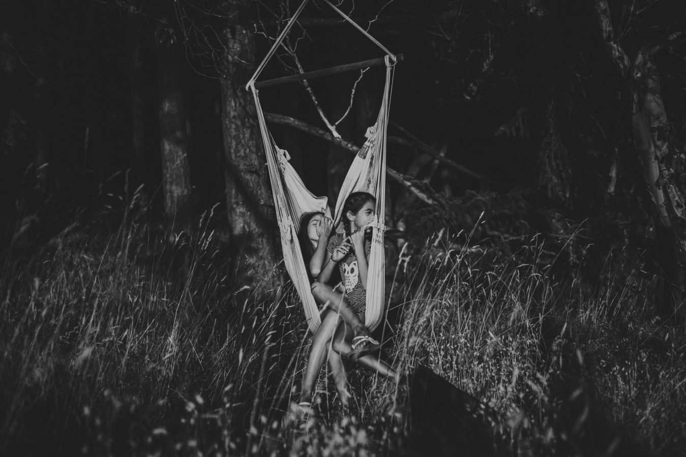 two kids squished in a hammock with the forest behind them