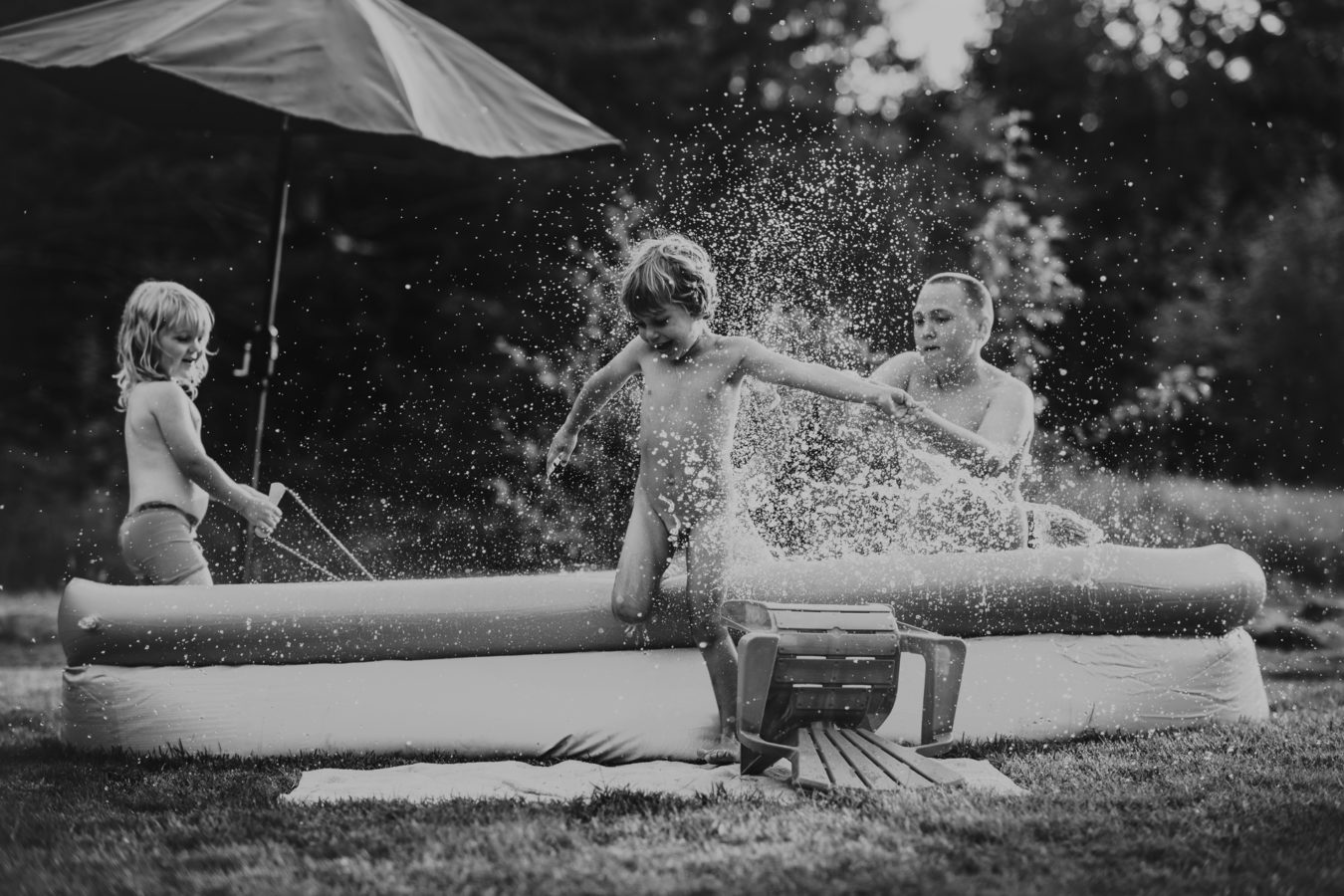 three kids splashing and playing in a small outdoor pool