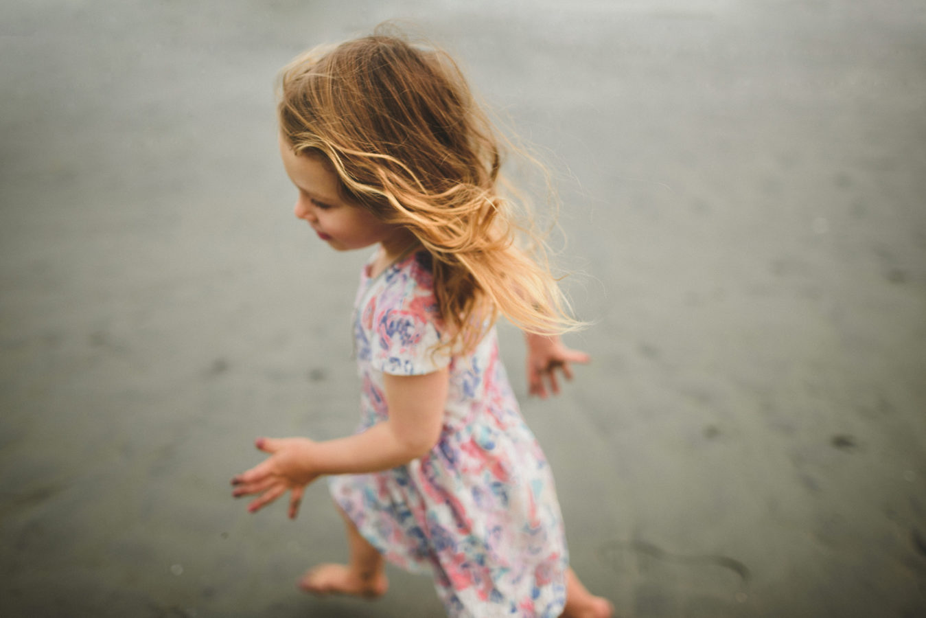 little girl running on the beach with her hair tossed behind her
