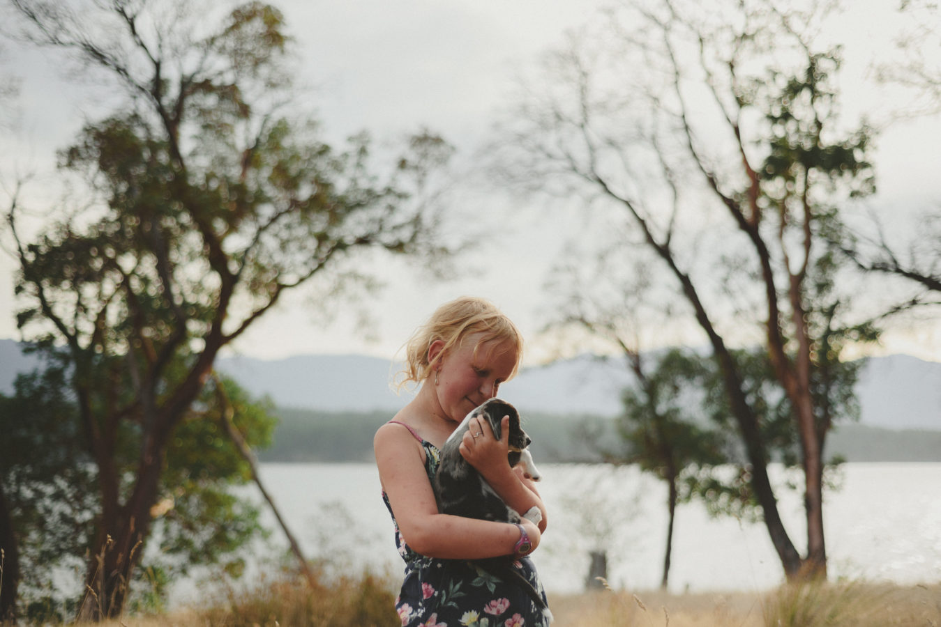 girl holding a puppy with trees and ocean behind her