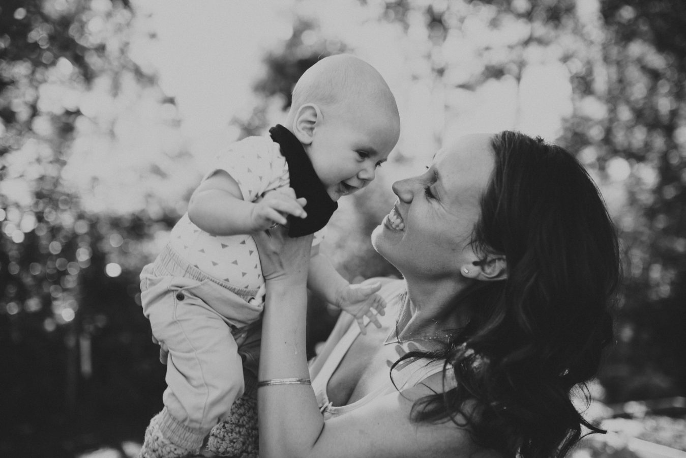mom smiling at her toddler who she's holding up in the air above her