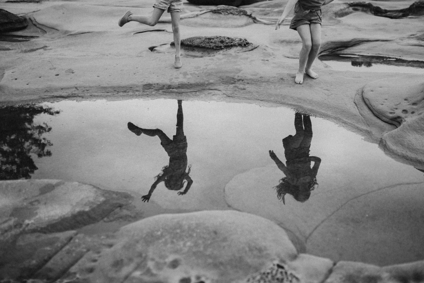 reflection of two kids dancing beside a tidal pool