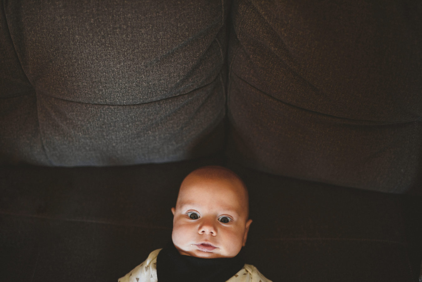 baby lying on a couch staring up into the camera