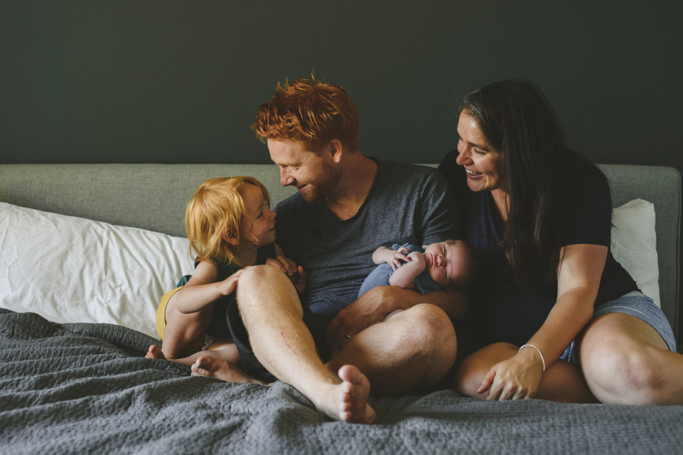 mom, dad, baby & kid snuggling on a bed