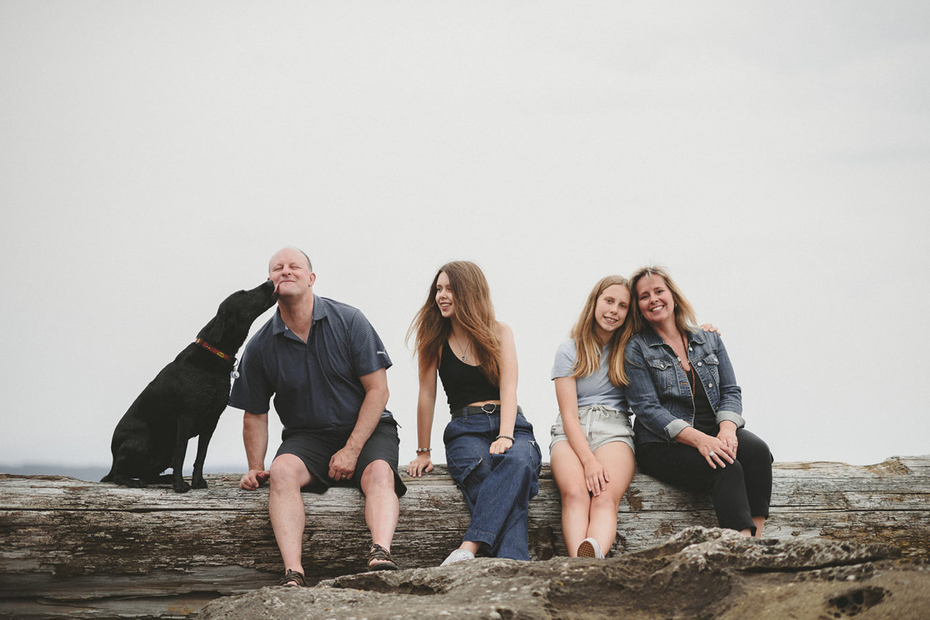 mom, dad, 2 teenagers and their dog sitting on a log laughing