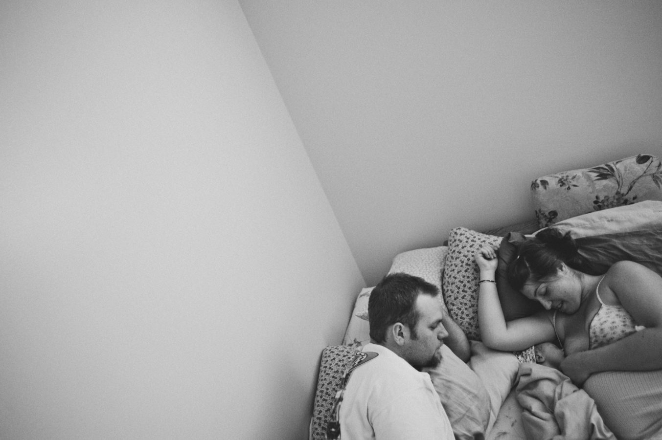 looking down at a woman breastfeeding her newborn snuggled in next to her husband