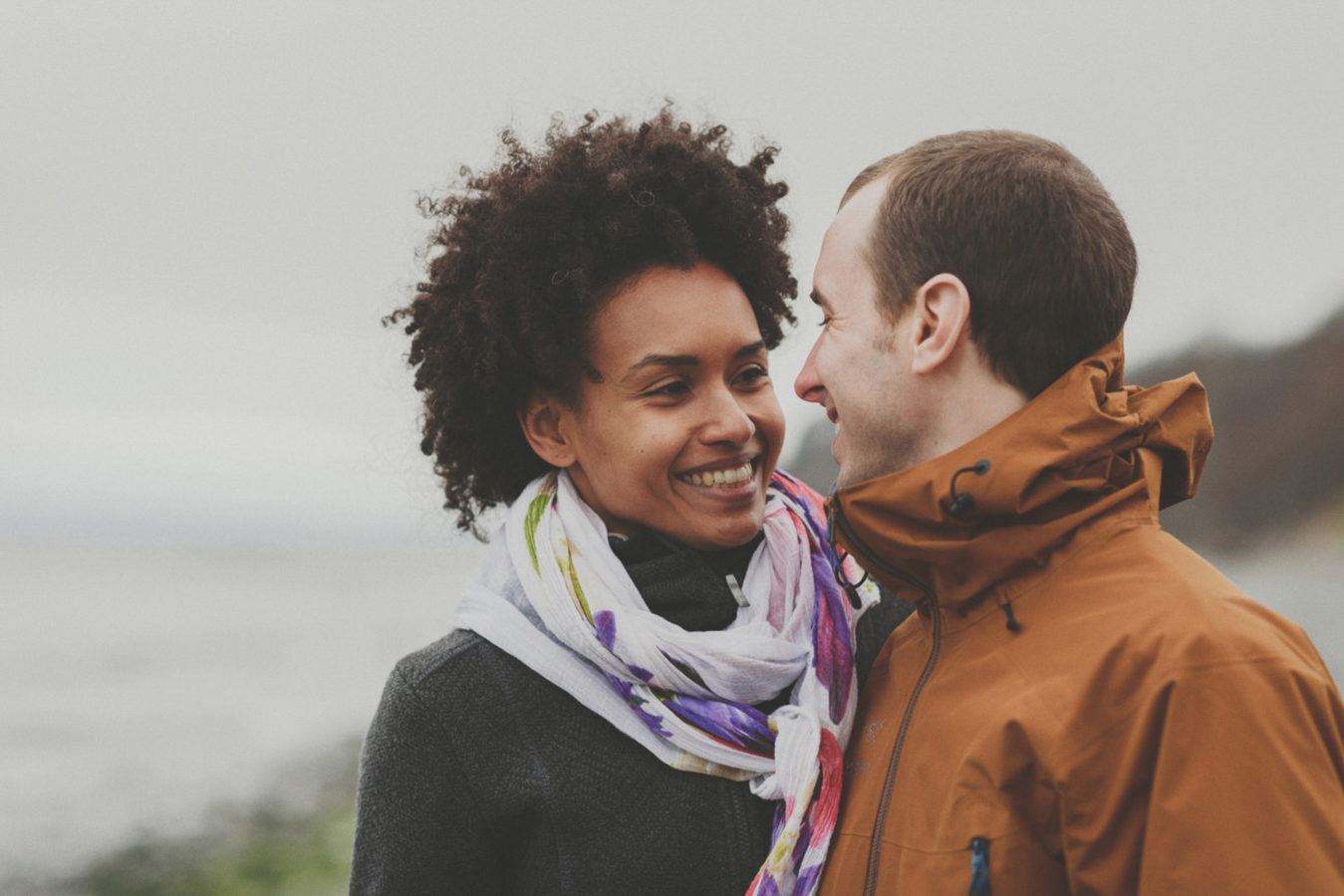 mixed race couple smiling at one another at the edge of the ocean