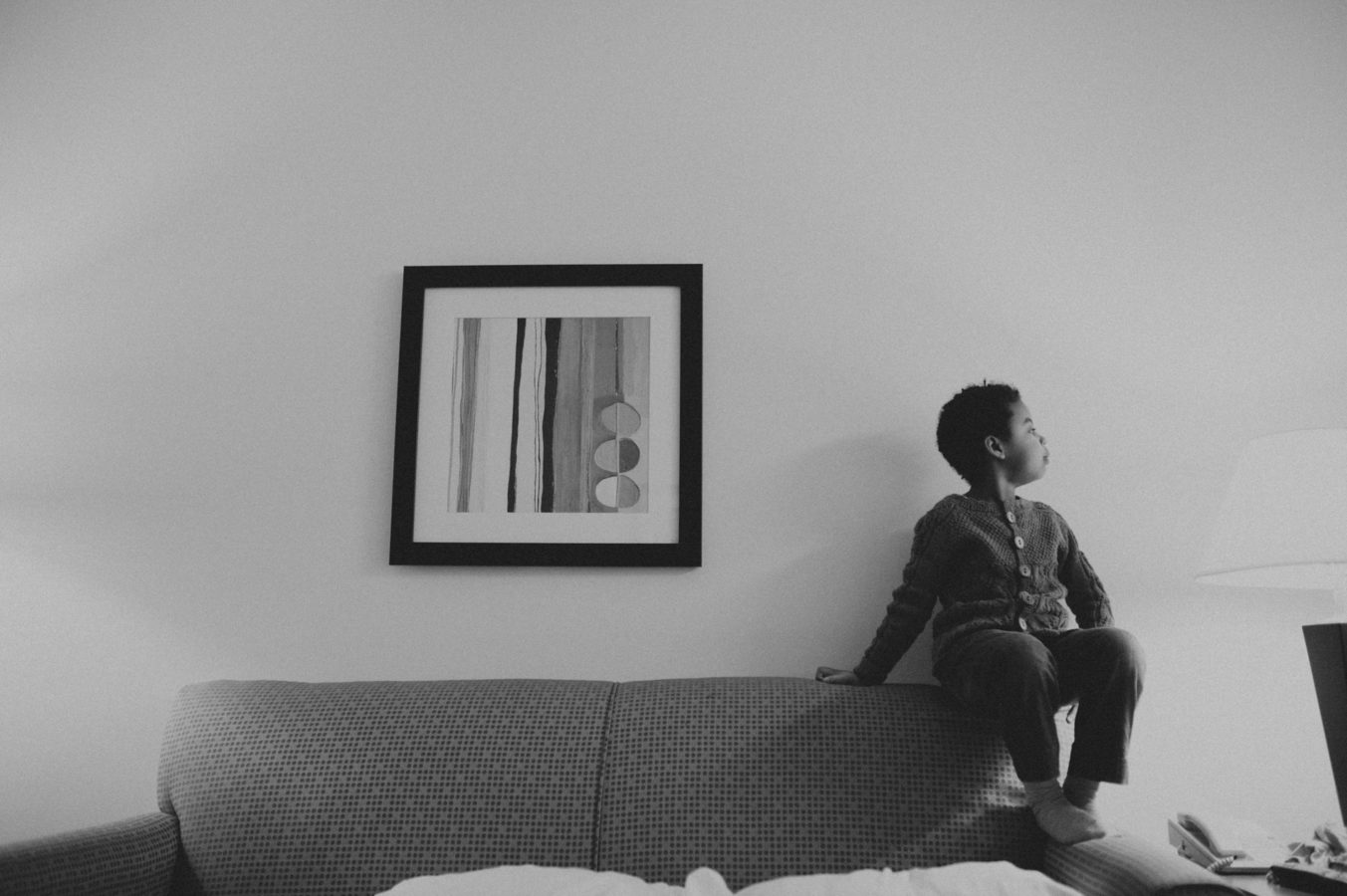 young Black girl sitting on the arm of a couch with a painting beside her on the wall