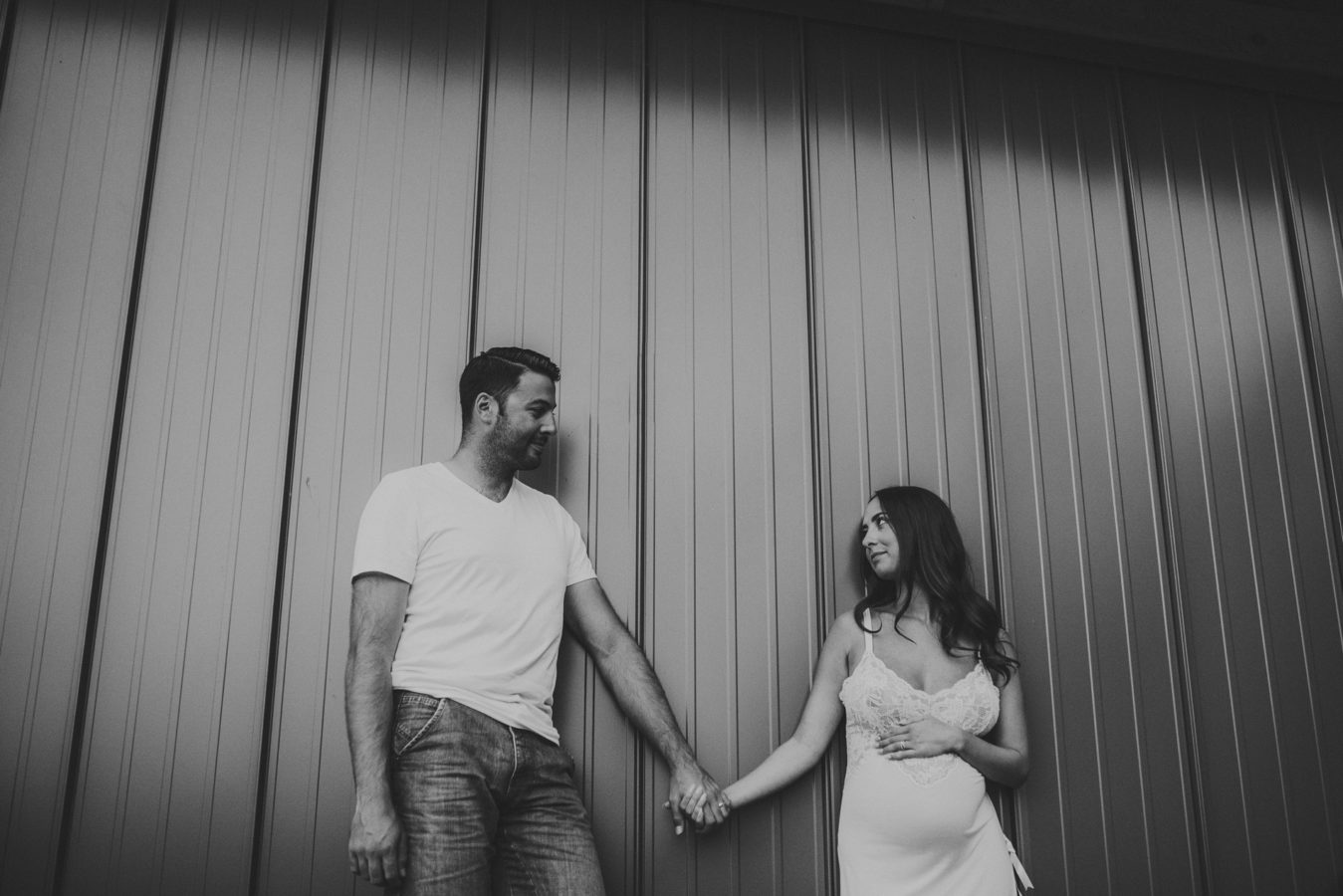 pregnant woman and her husband leaning up against a metal wall holding hands