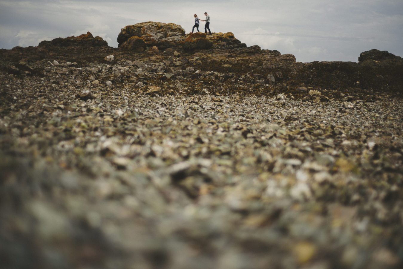 couple walking along a rocky area on the beach with the beach out of focus in the foreground