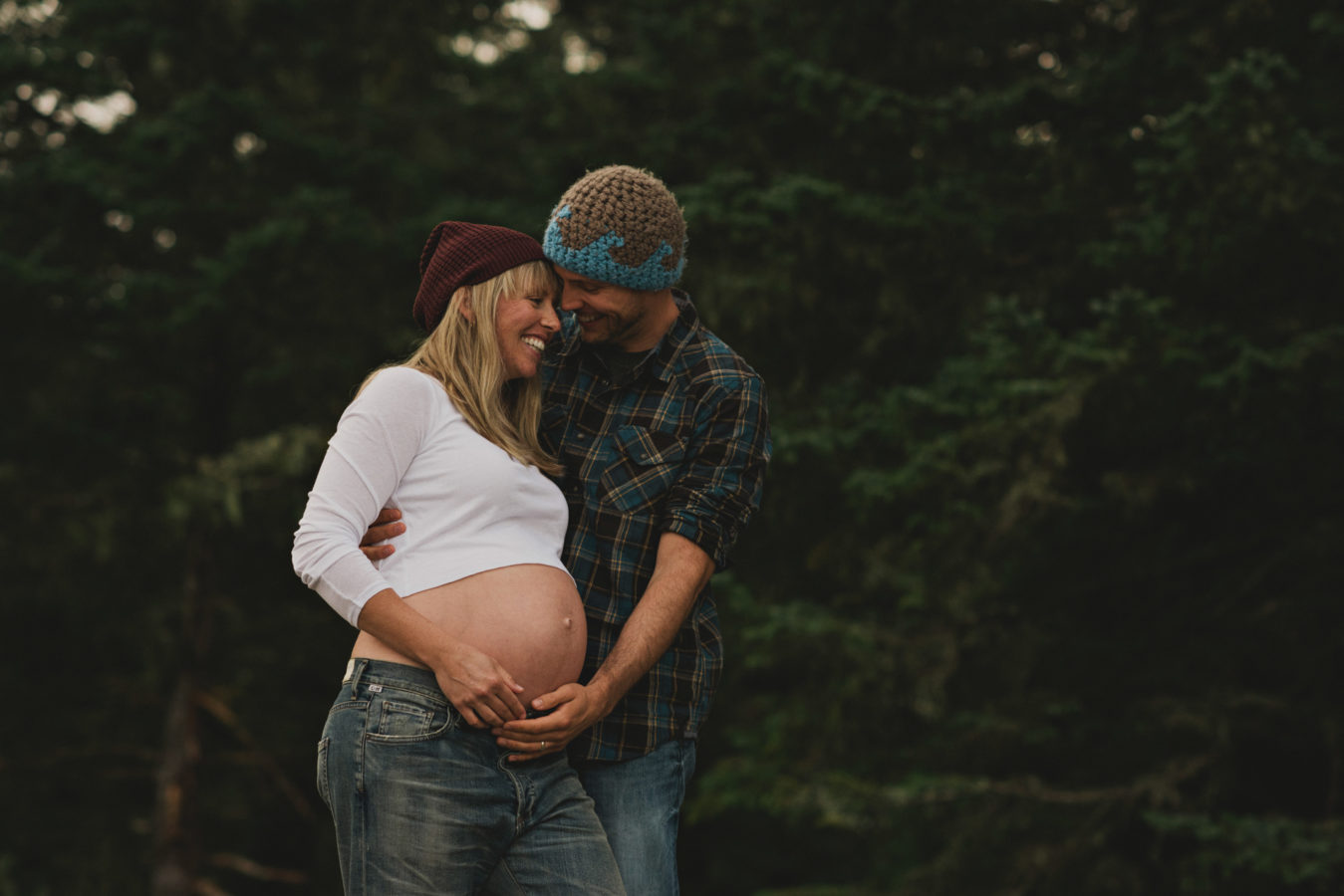 man holding his pregnant wife's belly set against the dark forest