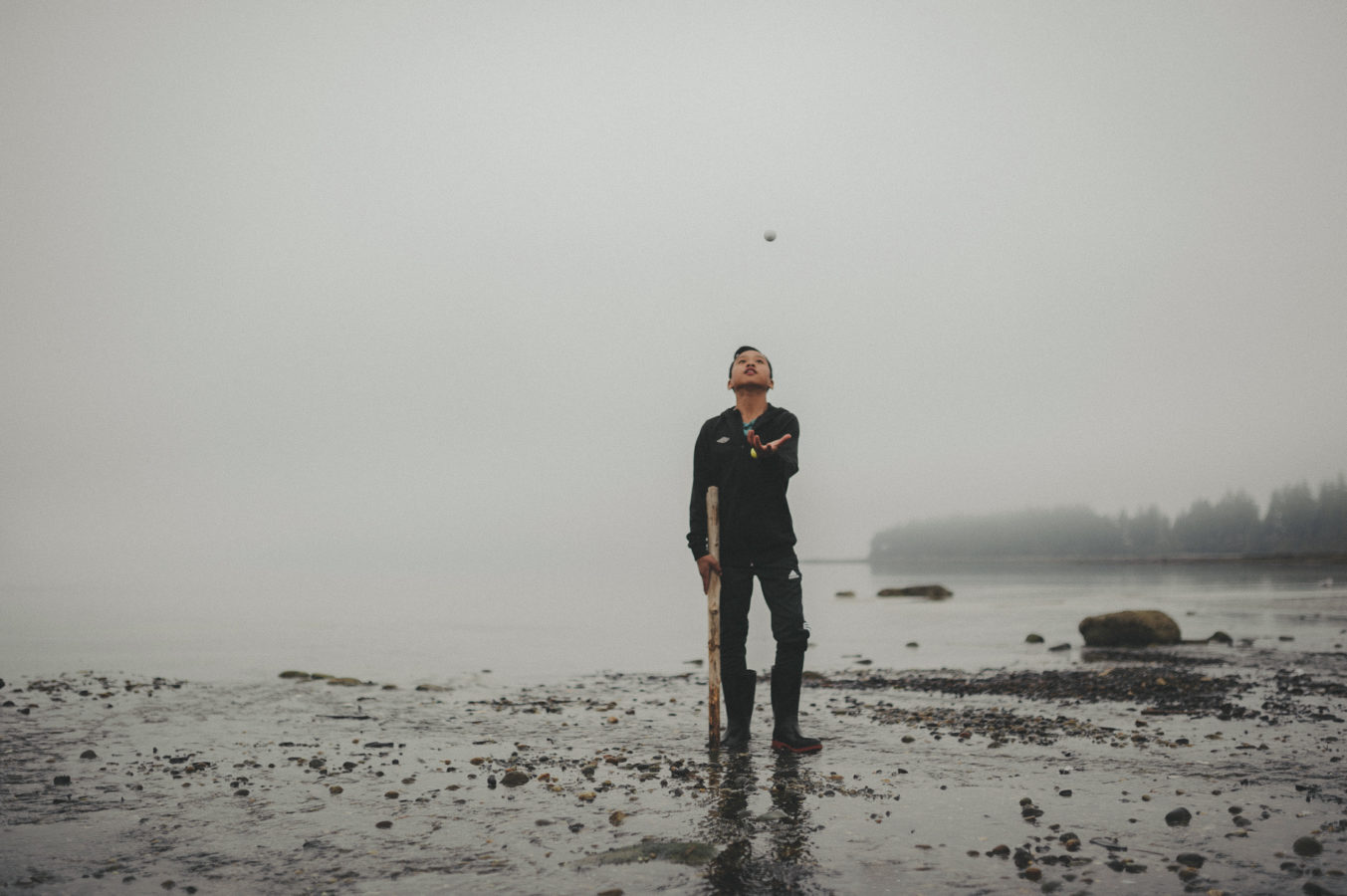 photo of a boy tossing a rock in the air on a foggy beach