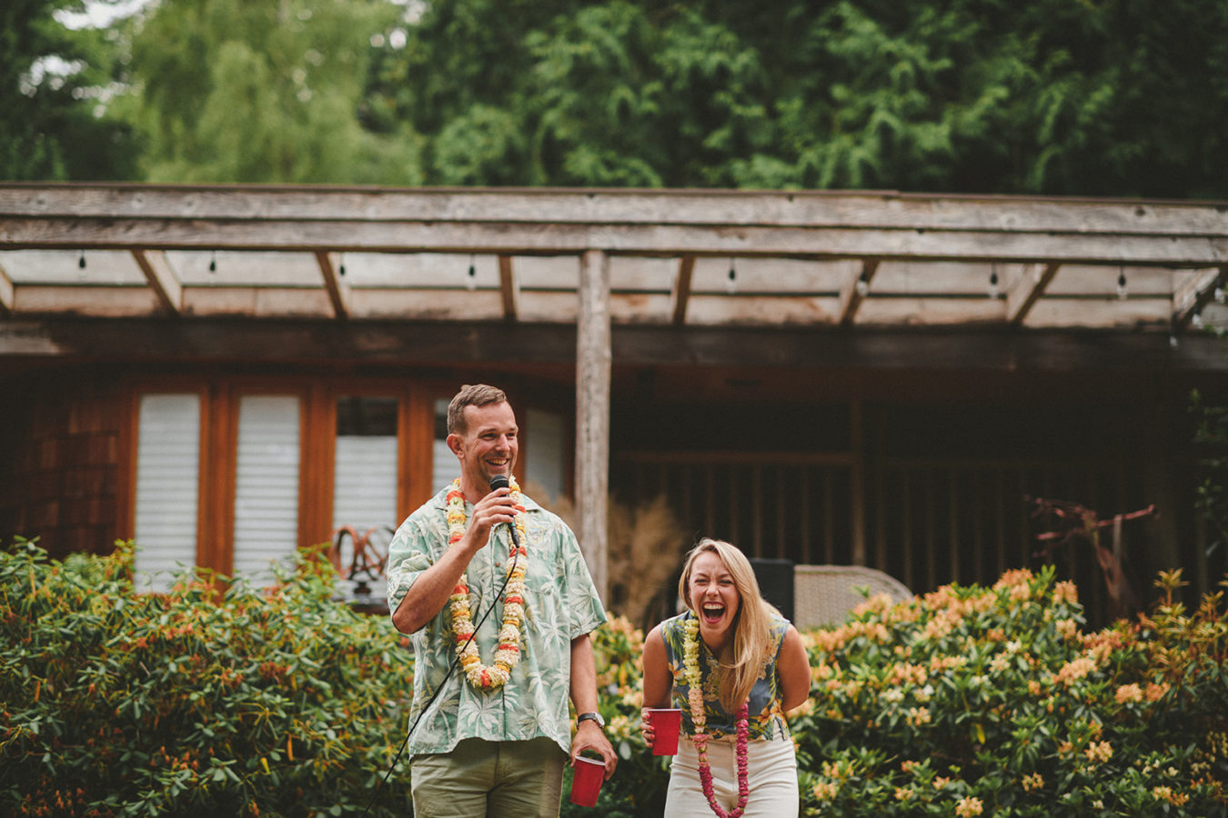 man talking into a microphone and his wife laughing beside him in front of a west coast home
