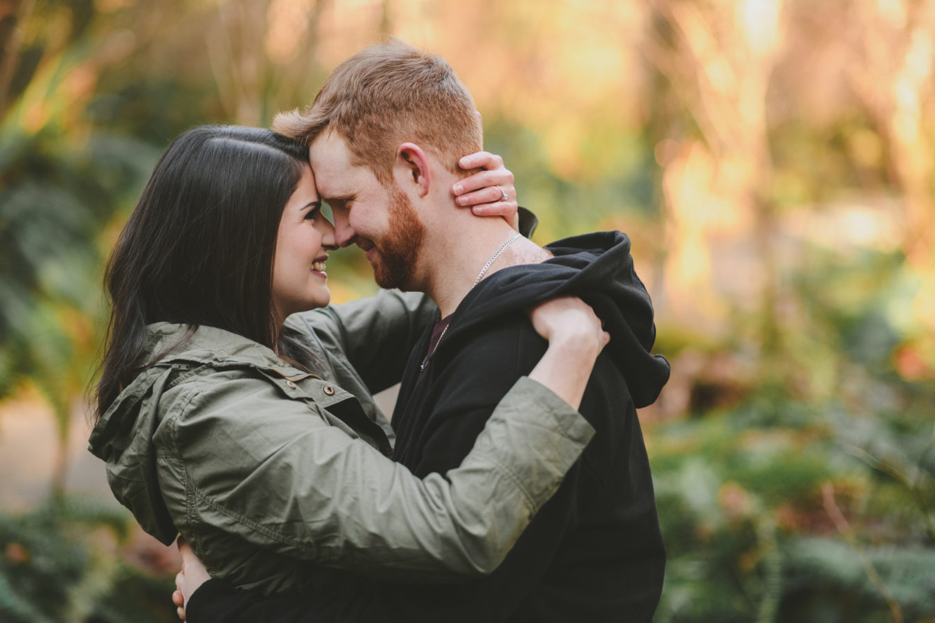 man and woman embracing and smiling with the sunlit forest behind them