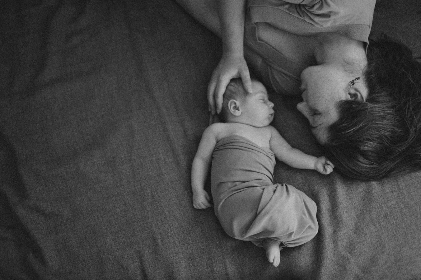 looking down on a woman and baby lying face to face on a bed