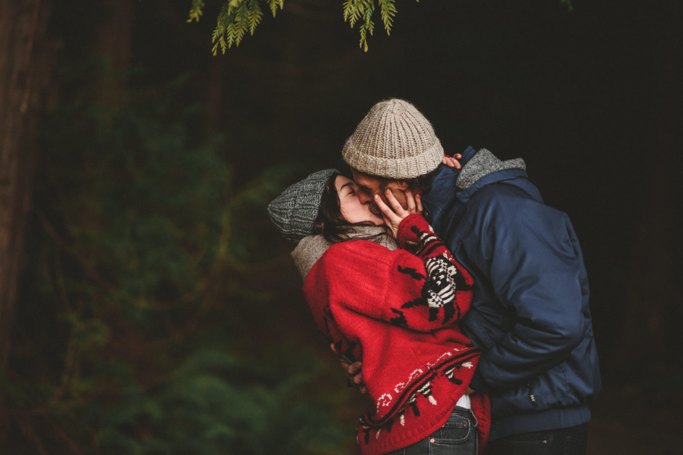 man and woman kissing with the dark forest behind them