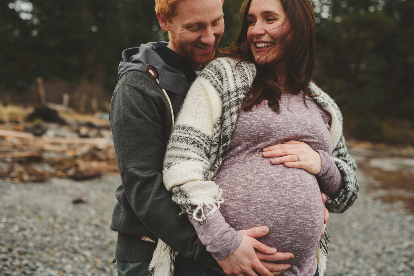 man and pregnant woman embracing and laughing on the beach