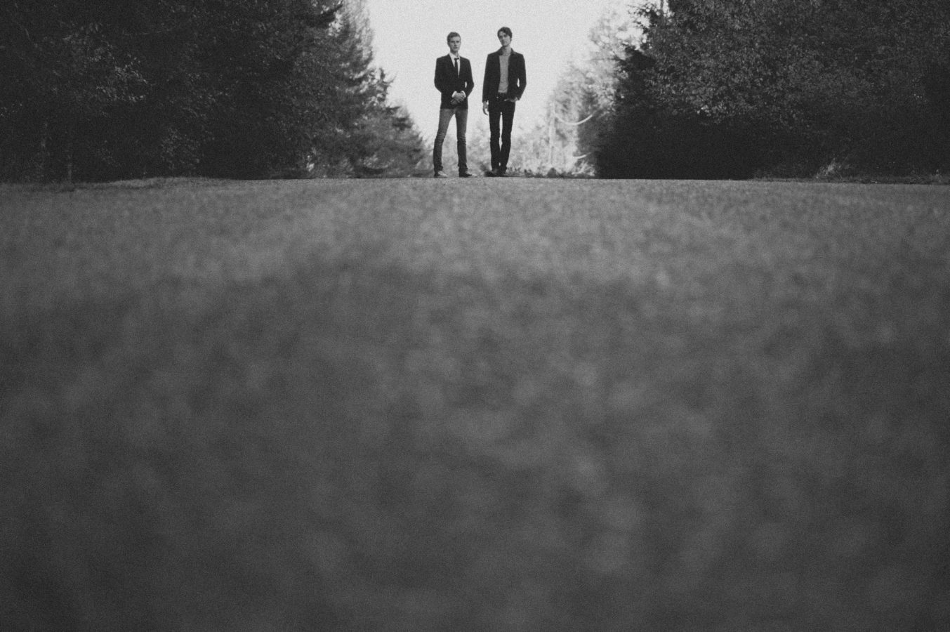 looking up a rural road at two men standing on the crest of a hill with the forest on either side of them