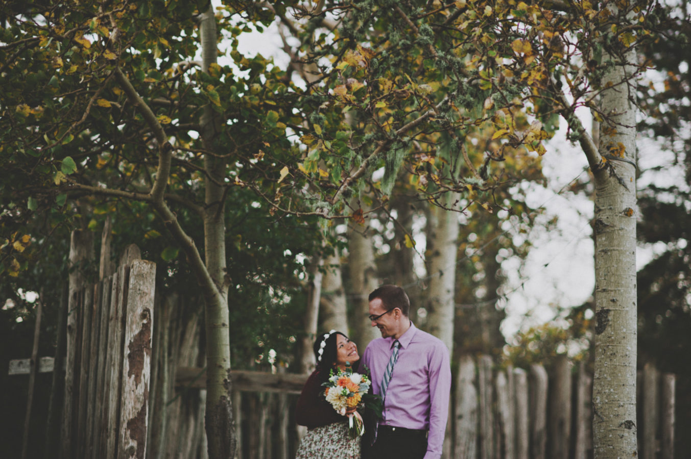 mixed race couple standing in front of a rustic fence smiling at one another on their wedding day