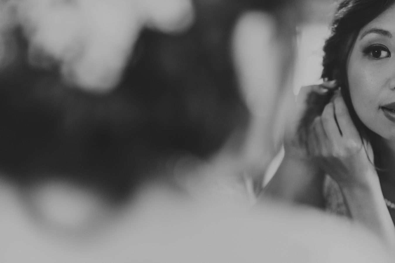 close up of bride's face reflected in a mirror as she is putting on her earrings