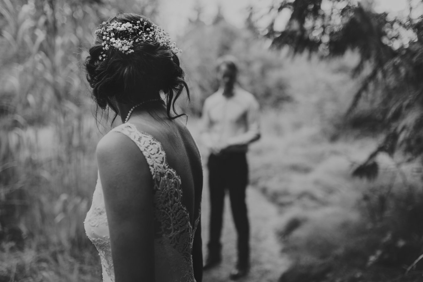 detail of a bride's back & hair with her groom standing in the background
