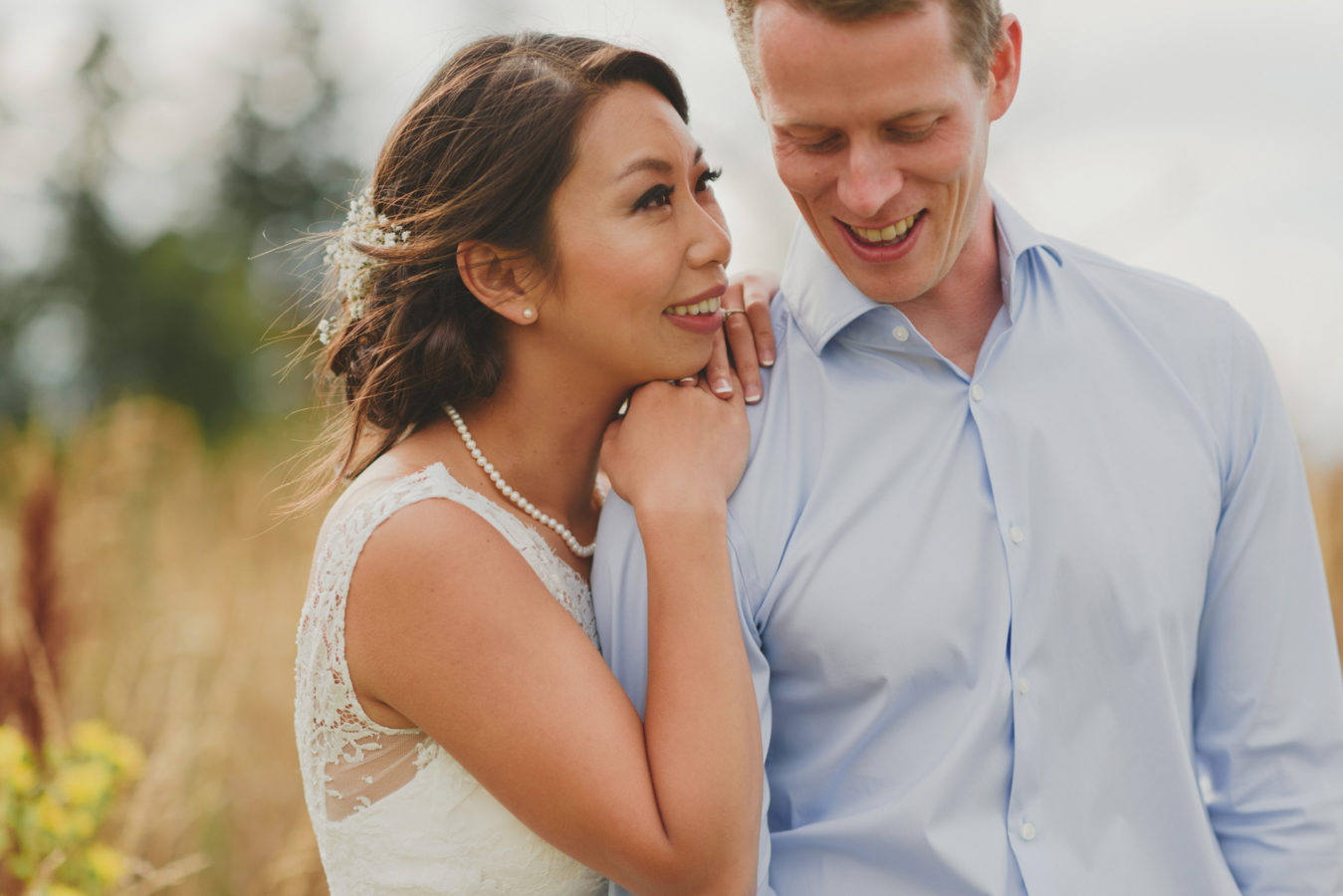 bride and groom cuddling and smiling in a sunlit field on their wedding day
