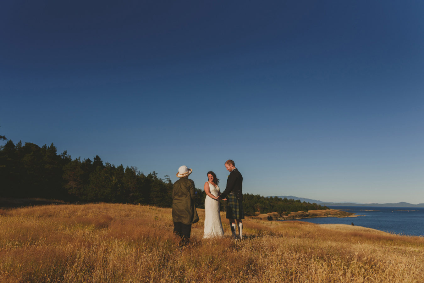 a bride and groom and officiant at their elopement ceremony on a grassy bluff overlooking the ocean