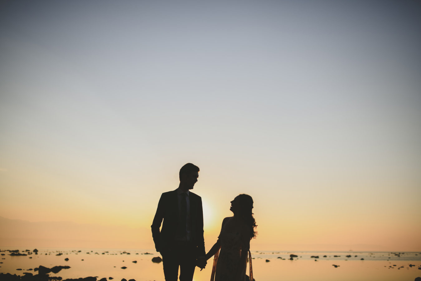 wedding couple silhoutted against the sunset at the ocean's edge