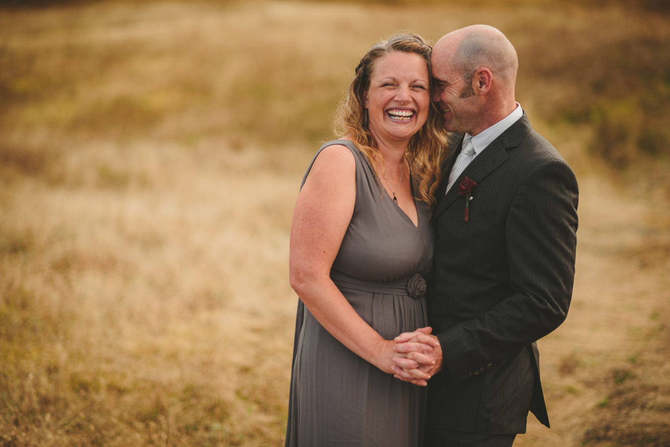 wedding couple laughing while embracing in a grassy field