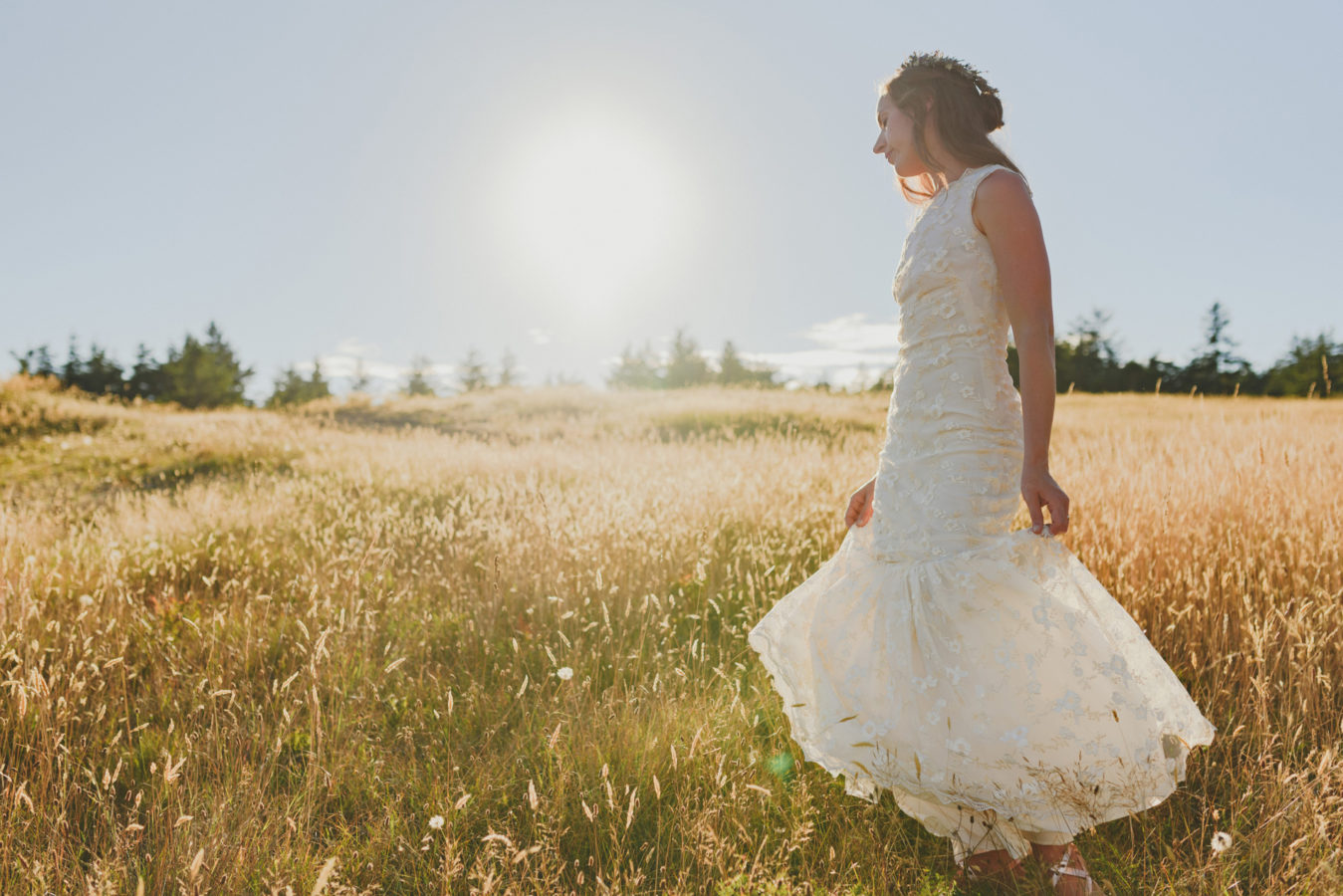 bride spinning in her wedding dress in a grassy field with the sunshine behind her