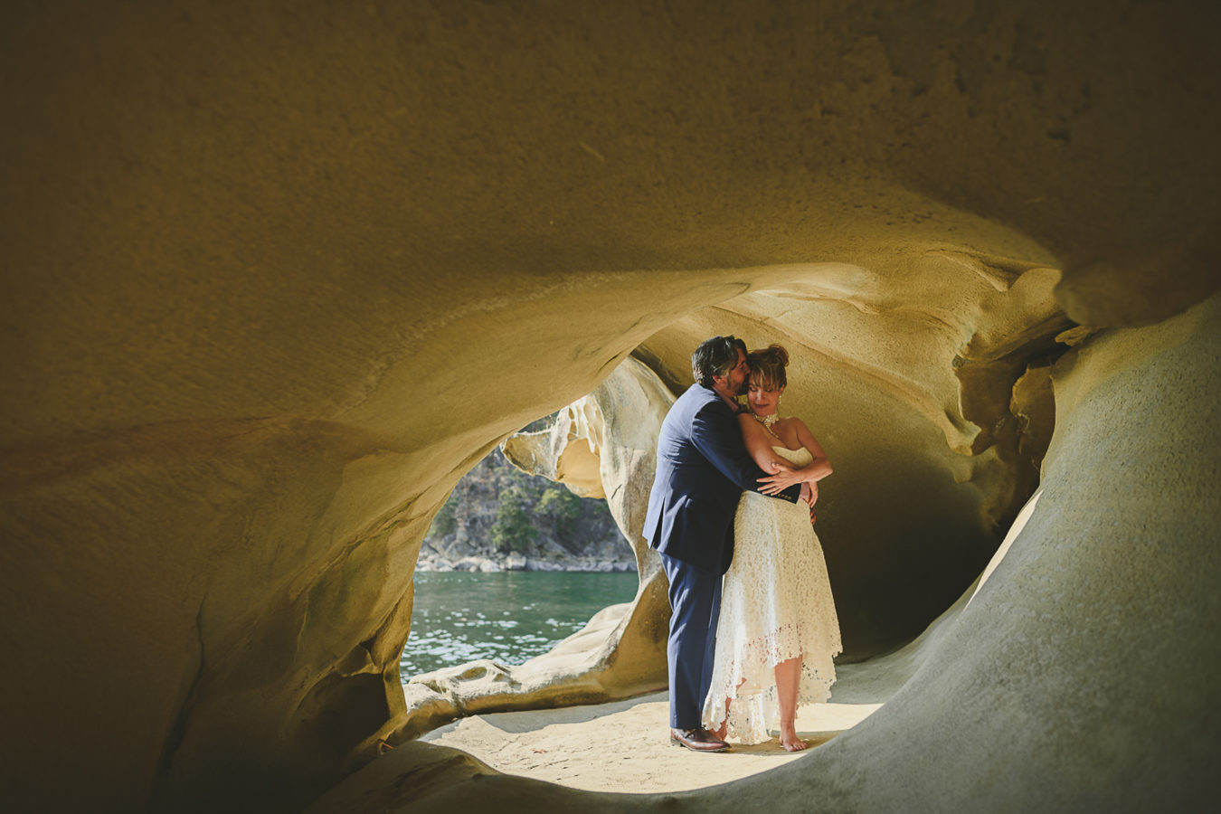 older bride and groom snuggled in a sandstone cave by the ocean's edge