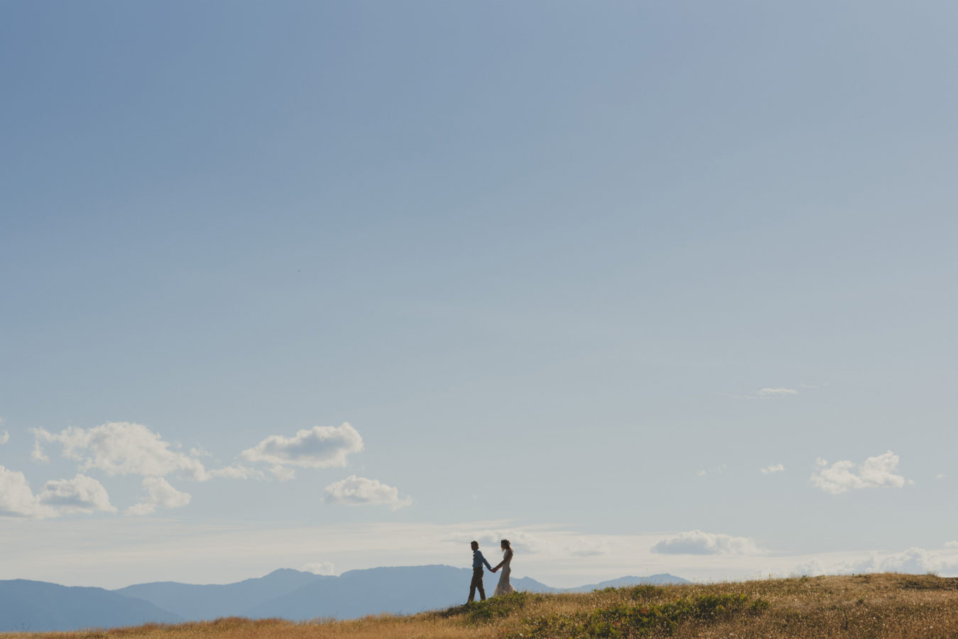 bride and groom walking along a grassy bluff under a big blue sky