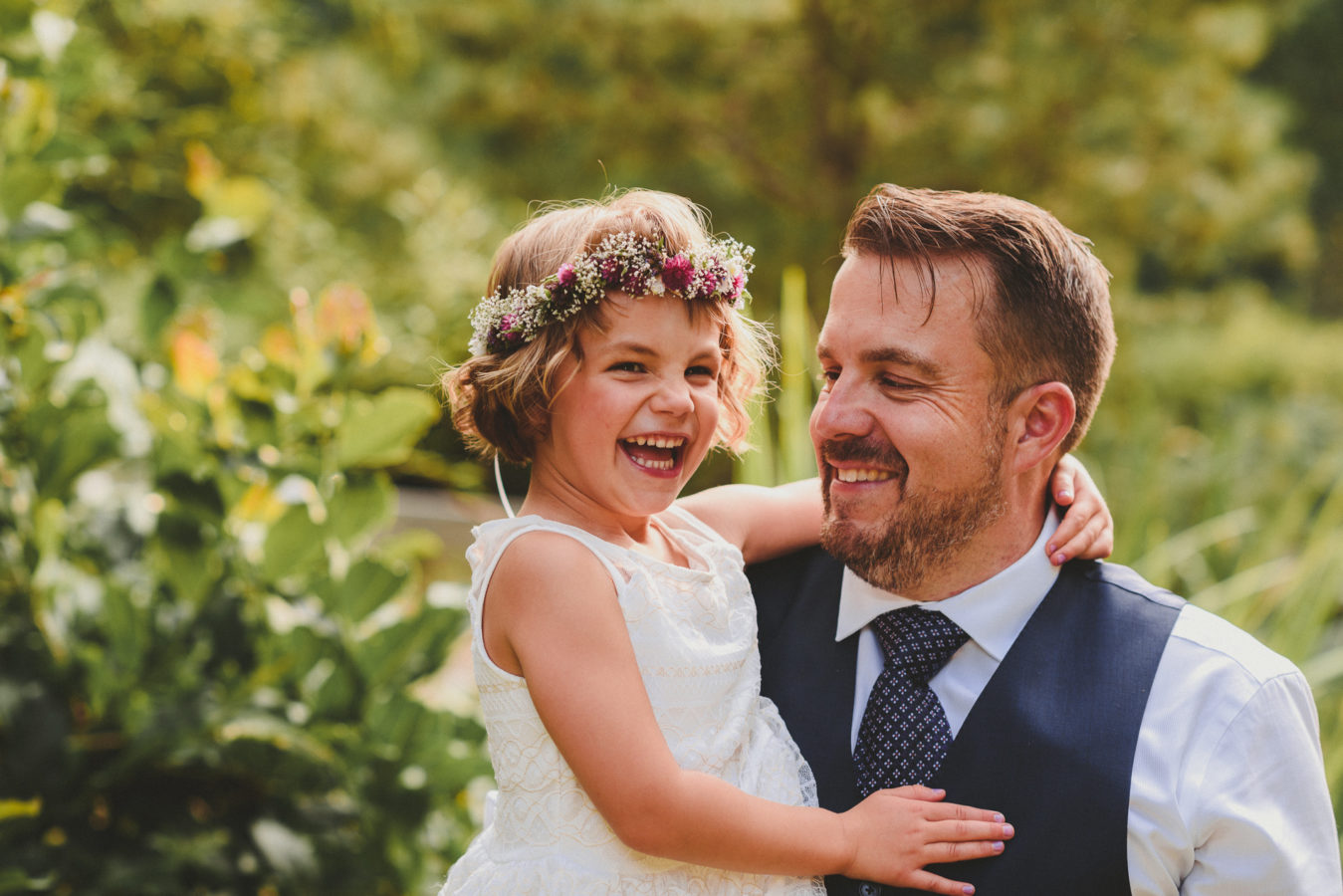 groom holding his daughter while she's laughing at his wedding