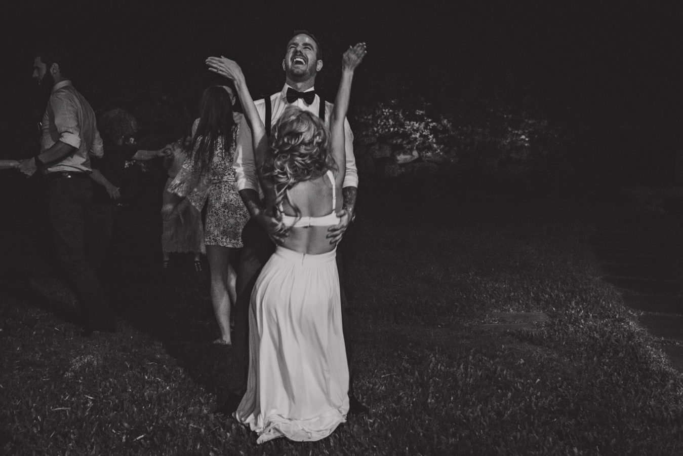 bride and groom dancing in a dark yard on their wedding day while he's throwing his head back laughing