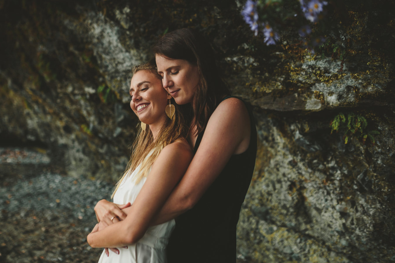 two brides snuggling next to a rocky bluff on the west coast