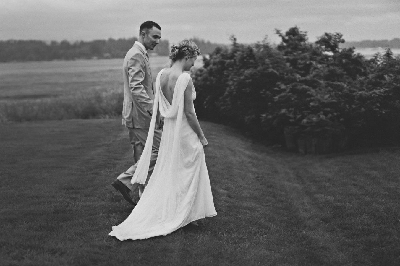 bride and groom walking hand in hand along the lawn at a seaside property